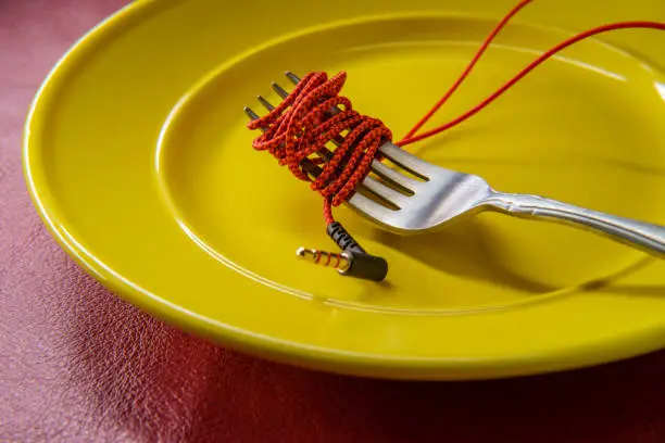 Red headphone wire wrapped around a fork on a plate like spaghetti as music consumption metaphor
