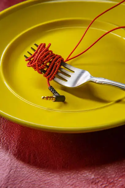 Red headphone wire wrapped around a fork on a plate like spaghetti as music consumption metaphor