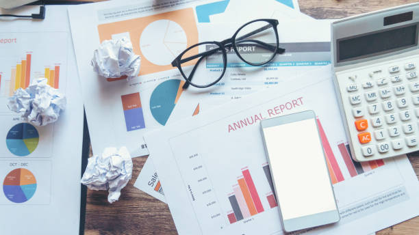 istock Home Office Desk Concept. Laptop, and calculator for accountant or bookkeeper plan annual budget report and tax. Computer, Crumpled paper, smartphone, and pen placed on wooden table. 1265254807