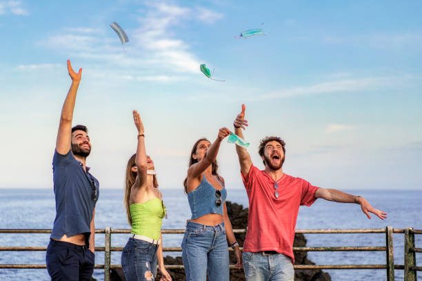 coronavirus quarantine and lockdown finished concept: young happy people celebrating the victory against virus with masks and hands up to the sky. Covid-19 pandemic ended. stock photo