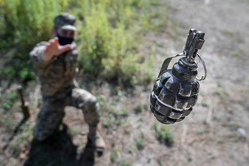 Grenade in flight with safety pin. A soldier in a mask threw a grenade, top view, focus on the grenade. open-wheel single-seater car grenade in flight.