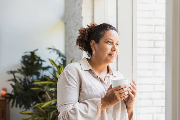 istock Mid adult woman daydreams while looking through window 1265260445