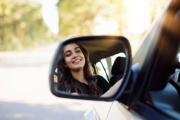 retrato de una joven conductora a través del espejo retrovisor de un coche moderno en una carretera por la noche - rear view mirror car mirror sun fotografías e imágenes de stock