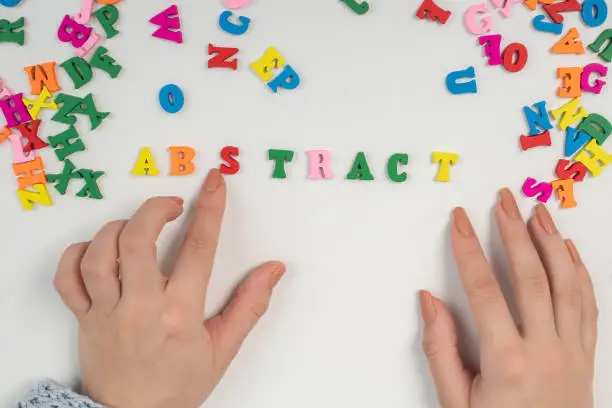 Photo of New ideas and fresh vision. Female hands lay out the word abstract from colored letters