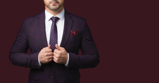 Well-dressed man wearing jacket and tie isolated on dark red background. Sharp dressed man in jacket and tie isolated on dark red background. Picture for advertising a men's clothing store. A symbol of success and masculinity metrosexual stock pictures, royalty-free photos & images