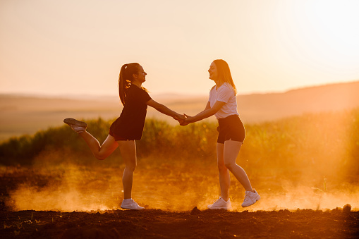 Copy space shot of two young women holding hands and jumping in the field at sunset. Summer Fun