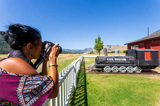 Midway, British Columbia, Canada - August 4, 2020: A woman tourist photographing the exterior view of the quaint Kettle River Museum located in the village of Midway, British Columbia, Canada. Located at \