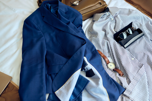 Men's businesswear with accessories on a bed in hotel room.