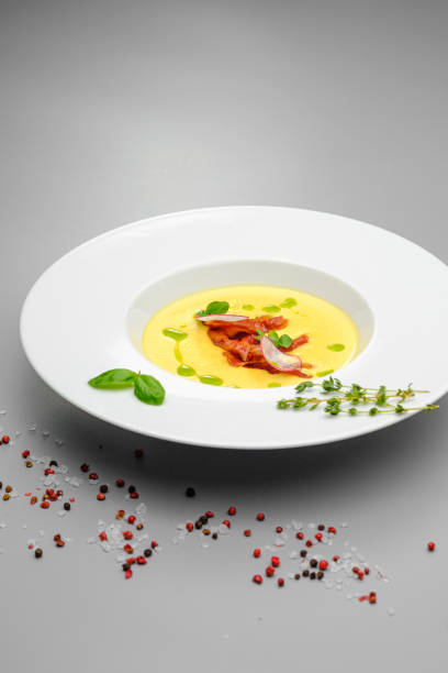 istock Corn cream soup with smoked meat in a white plate decorated with basil, on a gray background. The first course on the restaurant menu. 1265276012