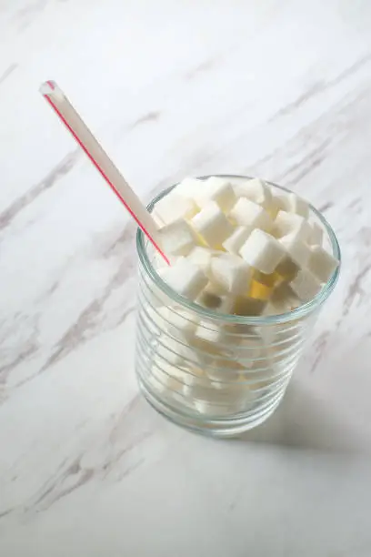 Conceptual sugar cubes in glass with striped soda straw diabetes conceptual metaphor