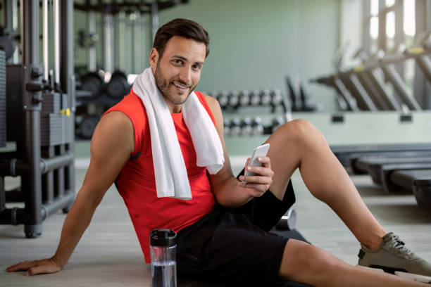 istock Happy athletic man using mobile phone while relaxing after sports training in a gym. 1265282457