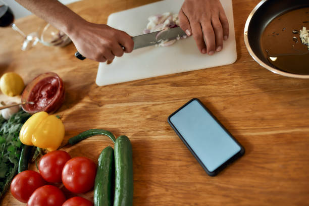 istock Close up of phone with blank screen on the table. Man cutting onion on chopping board, using smartphone app while cooking dinner. Healthy nutrition, technology concept 1265283366
