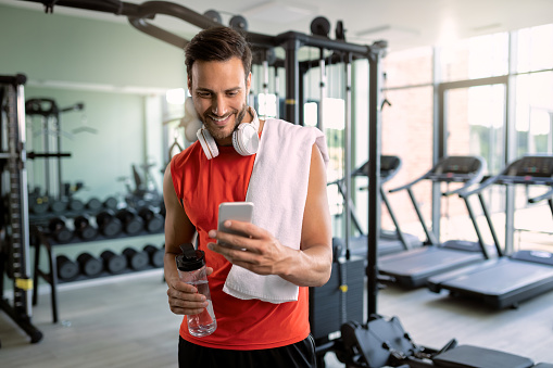 Young happy athlete using smart phone an reading text message in a gym.