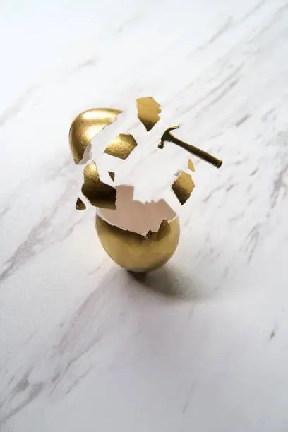 Tiny hammer breaks golden egg with shattered shell pieces action