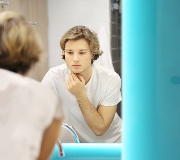 istock young man looking in the mirror,combing his hair,looking at problems on face 1265288823