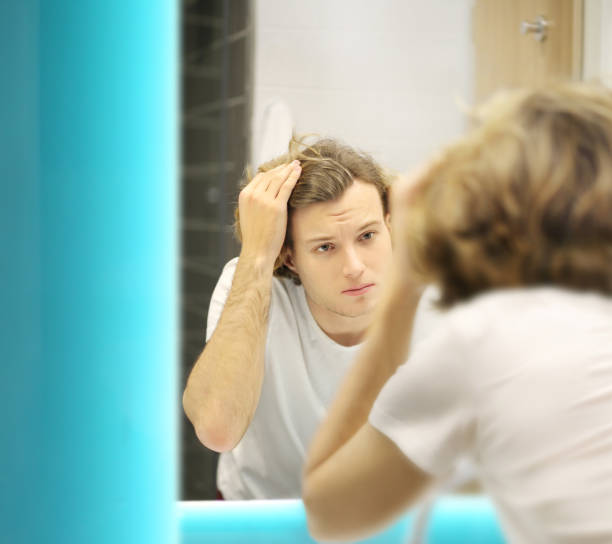 istock young man looking in the mirror,combing his hair,looking at problems on face 1265288829
