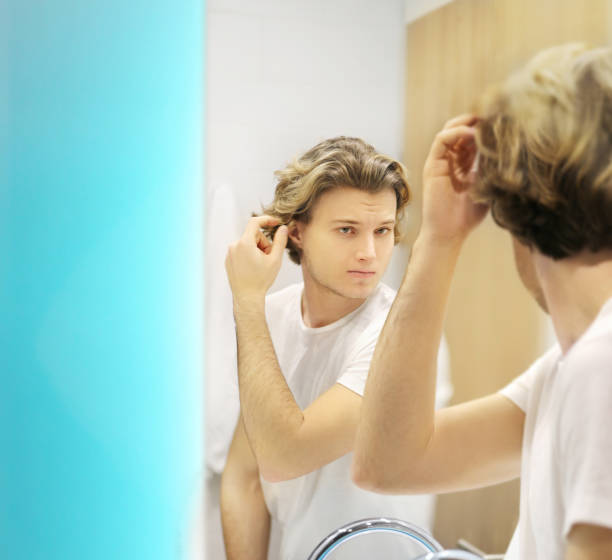 istock young man looking in the mirror,combing his hair,looking at problems on face 1265288834
