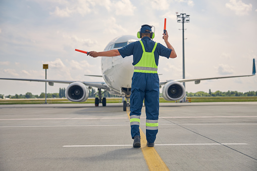 Man signaling the pilot with marshalling wands