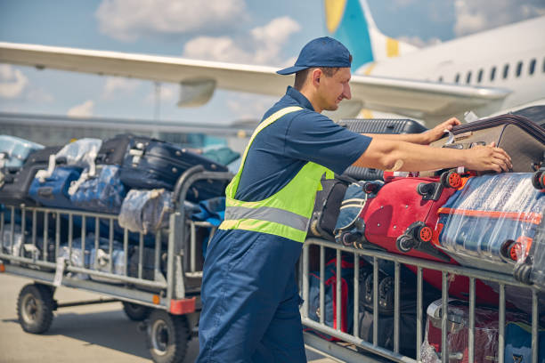 Airport male worker taking care of customer luggage Side view of a serious young Caucasian man in uniform loading suitcases from the airplane onto the carts luggage stock pictures, royalty-free photos & images