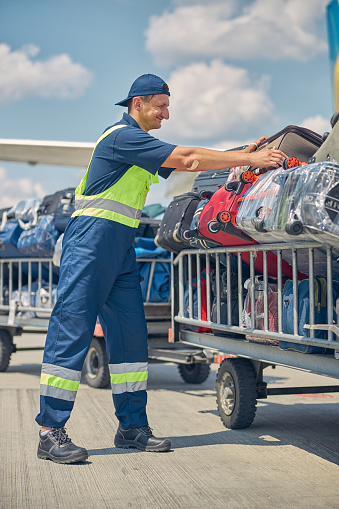 Full-length portrait of a serious baggage handler loading customer luggage on trolleys at the airdrome