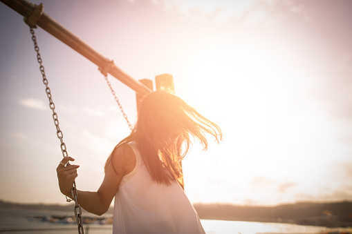 Young woman riding swing at suset beach