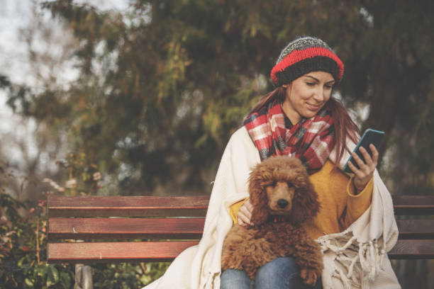 istock Woman using her smart phone while relaxing on a park bench with her dog on her lap 1265315617