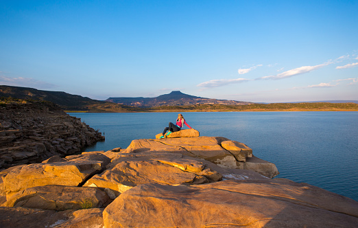 Abiquiu, NM: A laughing woman sitting and relaxing at Abiquiu Lake at dawn. Abiquiu, 50 miles north of Santa Fe, was home to Georgia O’Keeffe; she painted the flat-topped Pedernal Mountain in the distance.