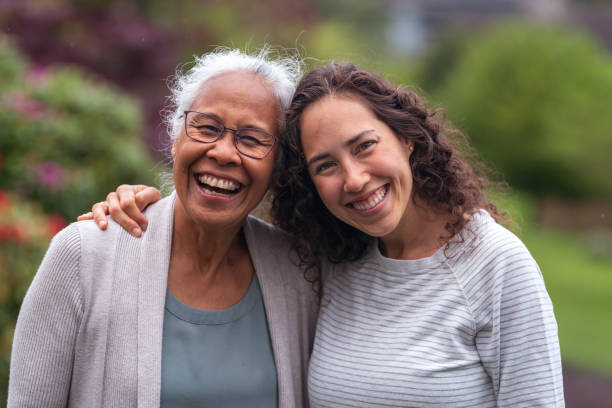 Mixed race mother and daughter walk and talk together outside A senior woman embraces her millennial Eurasian daughter as they happily walk through a natural parkland area and enjoy their time together. The daughter is smiling at the camera. adult age stock pictures, royalty-free photos & images
