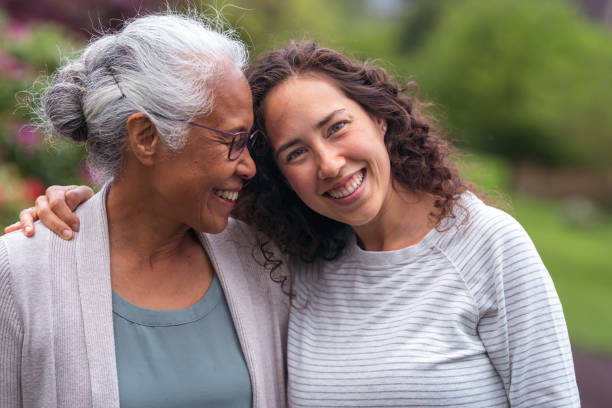 Mixed race mother and daughter walk and talk together outside A senior woman embraces her millennial Eurasian daughter as they happily walk through a natural parkland area and enjoy their time together. The daughter is smiling at the camera. legacy concept stock pictures, royalty-free photos & images