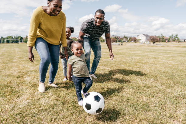 moments heureux de famille - enfants jouant au football avec des parents - family with two children family park child photos et images de collection