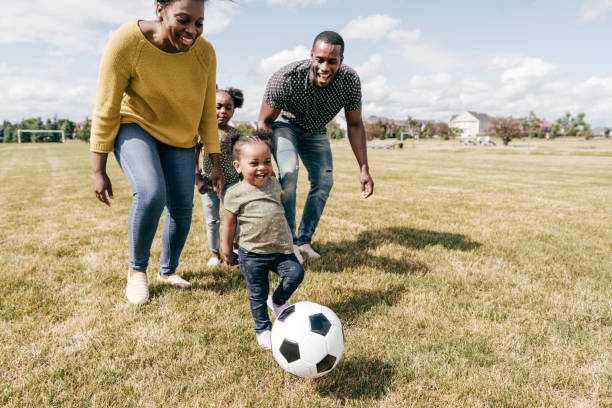 momenti felici in famiglia - bambini che giocano a calcio con i genitori - spring child field running foto e immagini stock