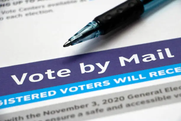 Closeup on a 'Vote by Mail' heading on a voter information paper and pen laying on top.