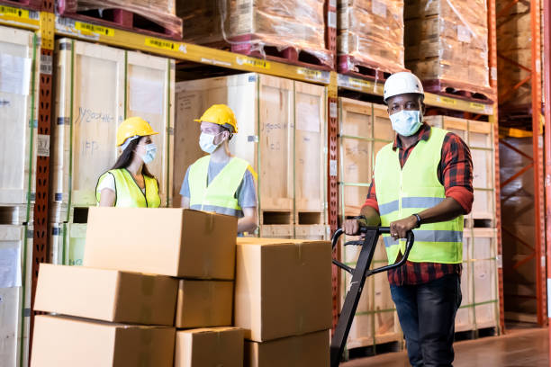 istock Group of diversity Workers wearing protective face mask working in factory warehouse. Black man pushing metal lathe cart with box parcel during covid 19 pandemic crisis. Logistic industry concept. 1265337618
