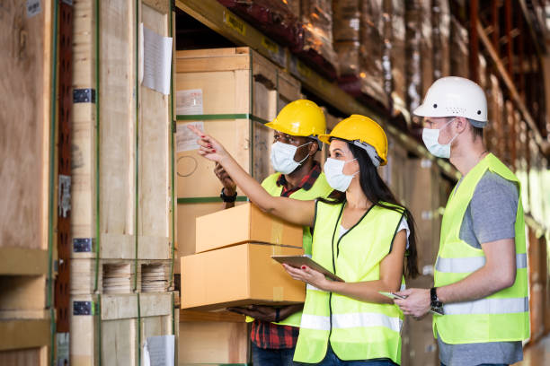 istock Group of diversity Workers wearing protective face mask working in factory warehouse. Black man holding box and other checking stock during covid 19 pandemic crisis. Logistic industry concept. 1265337674