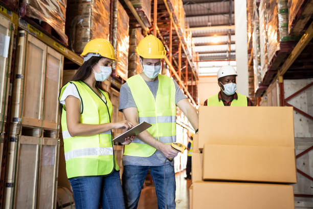 istock Group of diversity Workers wearing protective face mask working in factory warehouse. Black man pushing metal lathe cart with box parcel during covid 19 pandemic crisis. Logistic industry concept. 1265337771