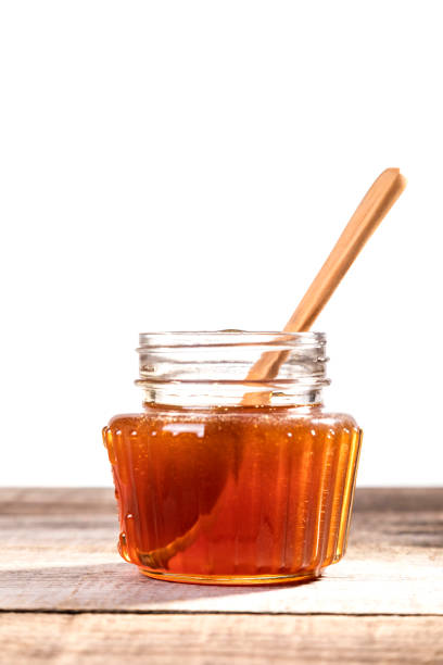 Honey dripping from the honey dipper into a glass jar. Close up. Healthy organic coarse honey dipping from the wooden honey spoon.