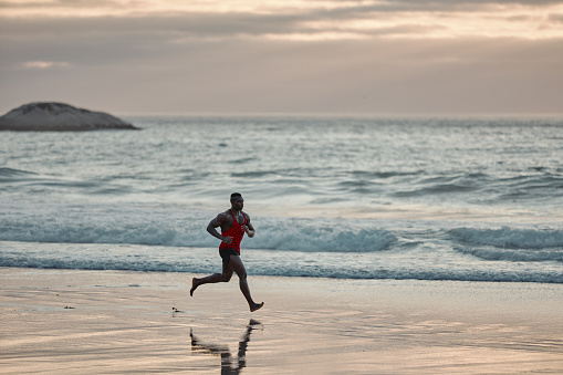 Shot of a muscular young man running at the beach