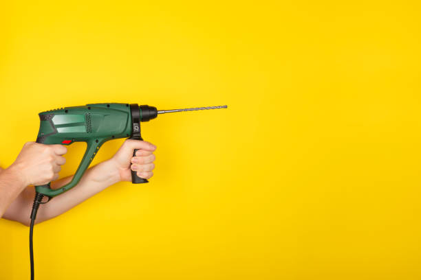 istock Male hands hold new Puncher or drill isolated on yellow background. 1265396669