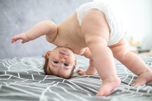 Baby standing upside down on a bed, attempting to stand or crawl