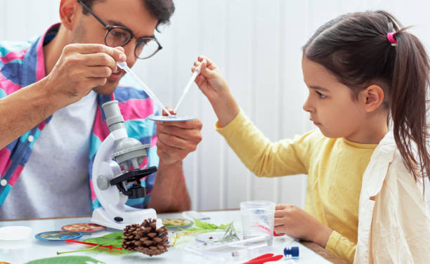 dad and little girl study chemistry lesson with microscope, mixing liquids in the flasks for lab experiment. father and his daughter working and exploring with the microscop. homeschooling concept. - microscop imagens e fotografias de stock