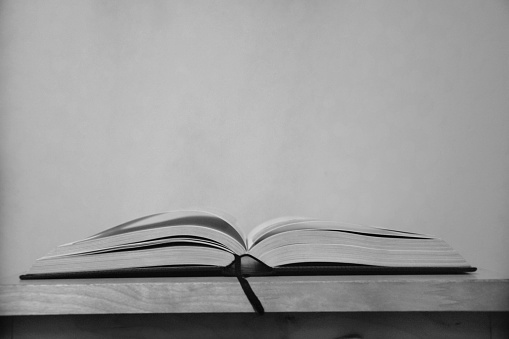 Black & white photo of a stack of books with a pen on top, reflected on a black table