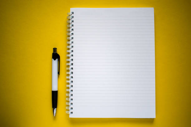 istock Flat lay of white and black pen and notepad on yellow background 1265436299