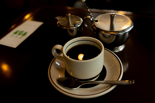 A cup and saucer filled with coffee on an old-fashioned Japanese coffee shop table.
retrospective coffee shop. Retro cups and saucers. Dark brown table.