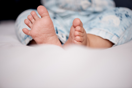 Tiny feet of newborn. Soft feet of baby on white blanket at home. Selective focus.