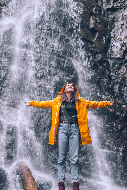 istock woman in yellow raincoat at autumn waterfall 1265438949