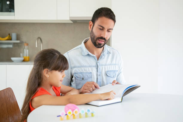 istock Cute little girl pointing at text and learning with dad 1265440123