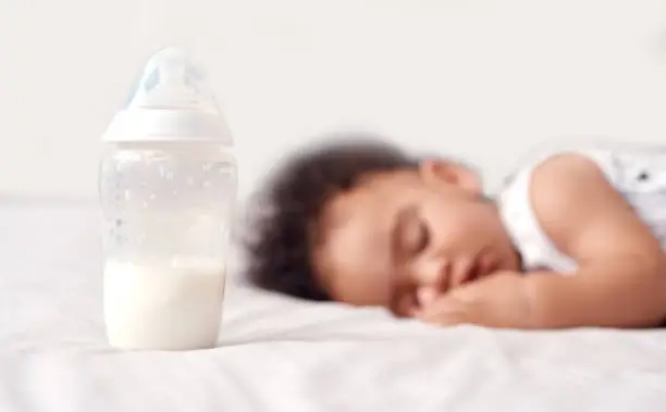Shot of an adorable baby boy sleeping with his bottle of milk on the bed at home