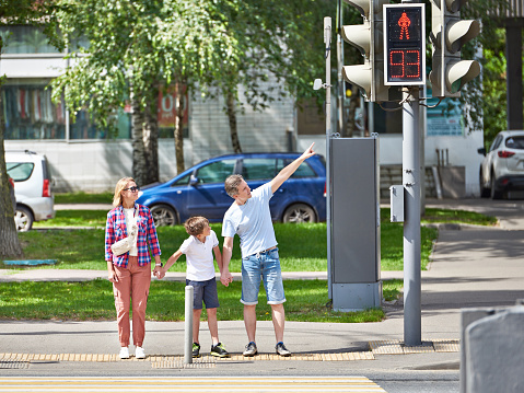 Family, woman, man and child cross the road at a pedestrian crossing