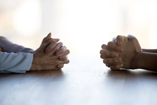 sluit omhoog geklemde vrouwelijke handen van twee zakenvrouwen onderhandel bij lijst - tegenspoed stockfoto's en -beelden