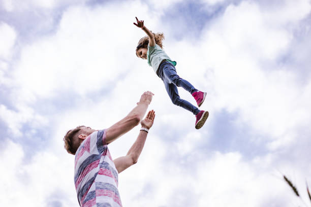 Happy little girl is up in the air flying. Her father is throwing her high. They are playing.